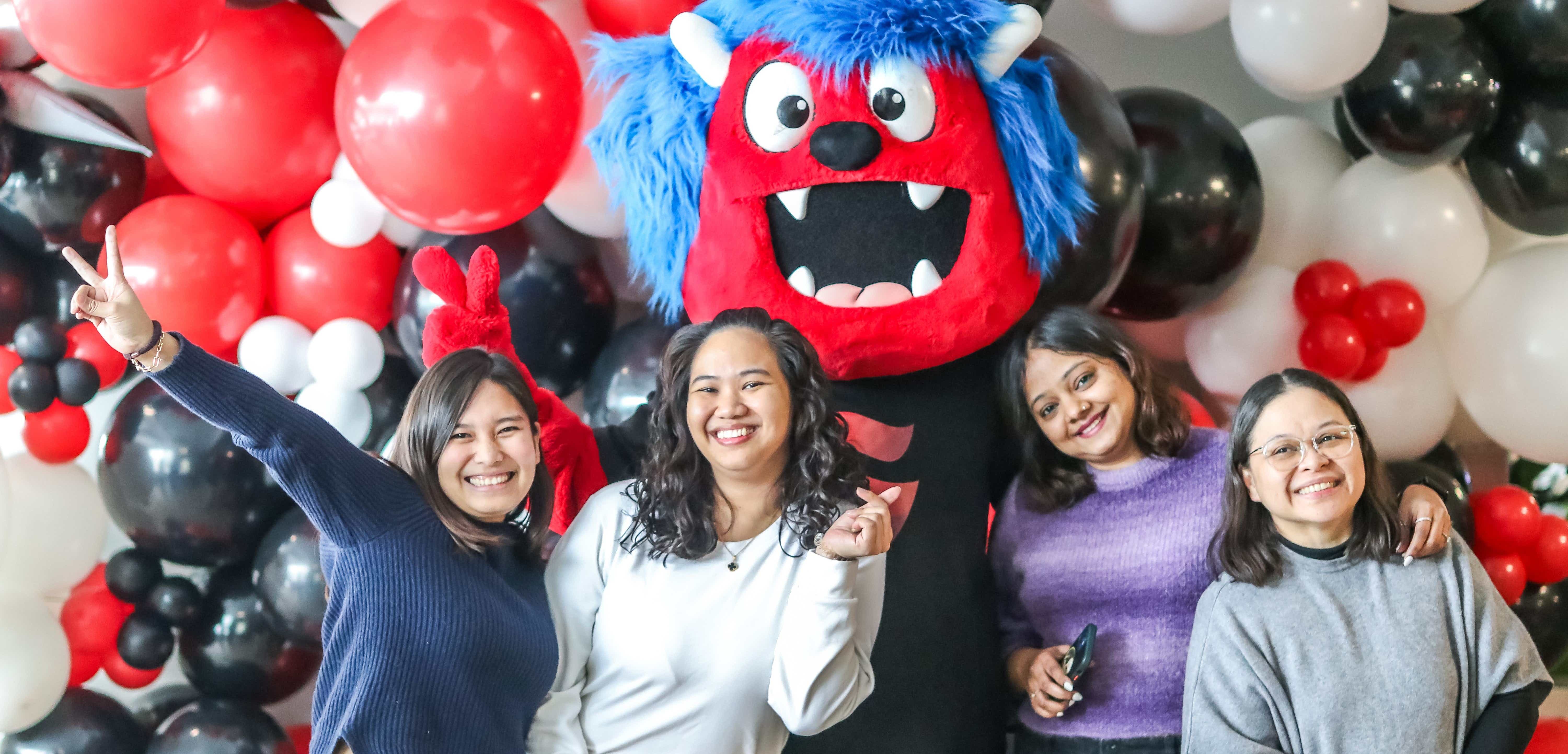 A group of students smile with SLC's mascot Storm in front of a balloon wall